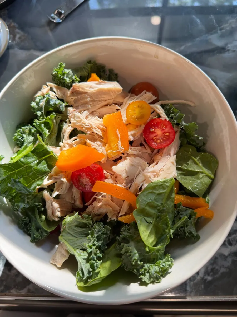 A simple bowl of kale and spinach topped with shredded chicken, cherry tomatoes, and sweet peppers