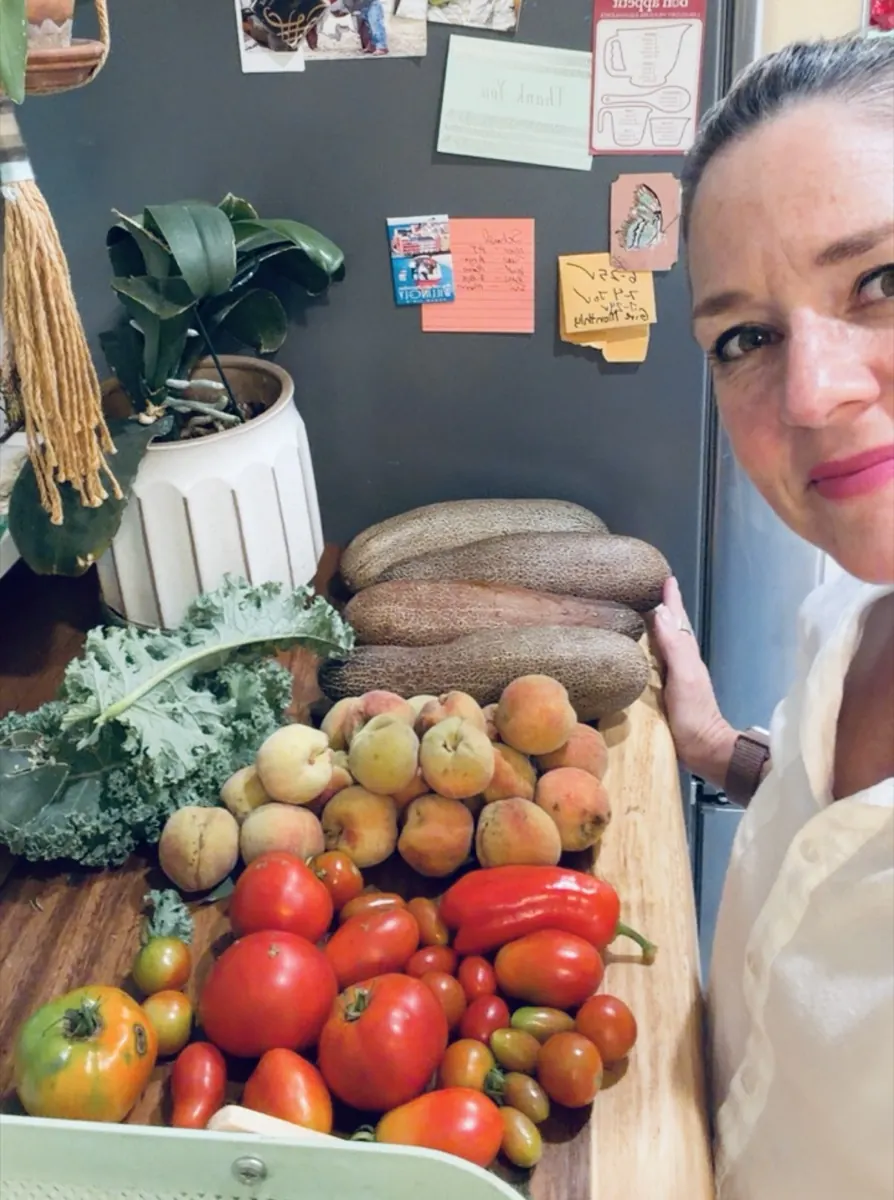 Anya Gossage in her kitchen with fresh tomatoes, peaches, peppers, and kale from her garden