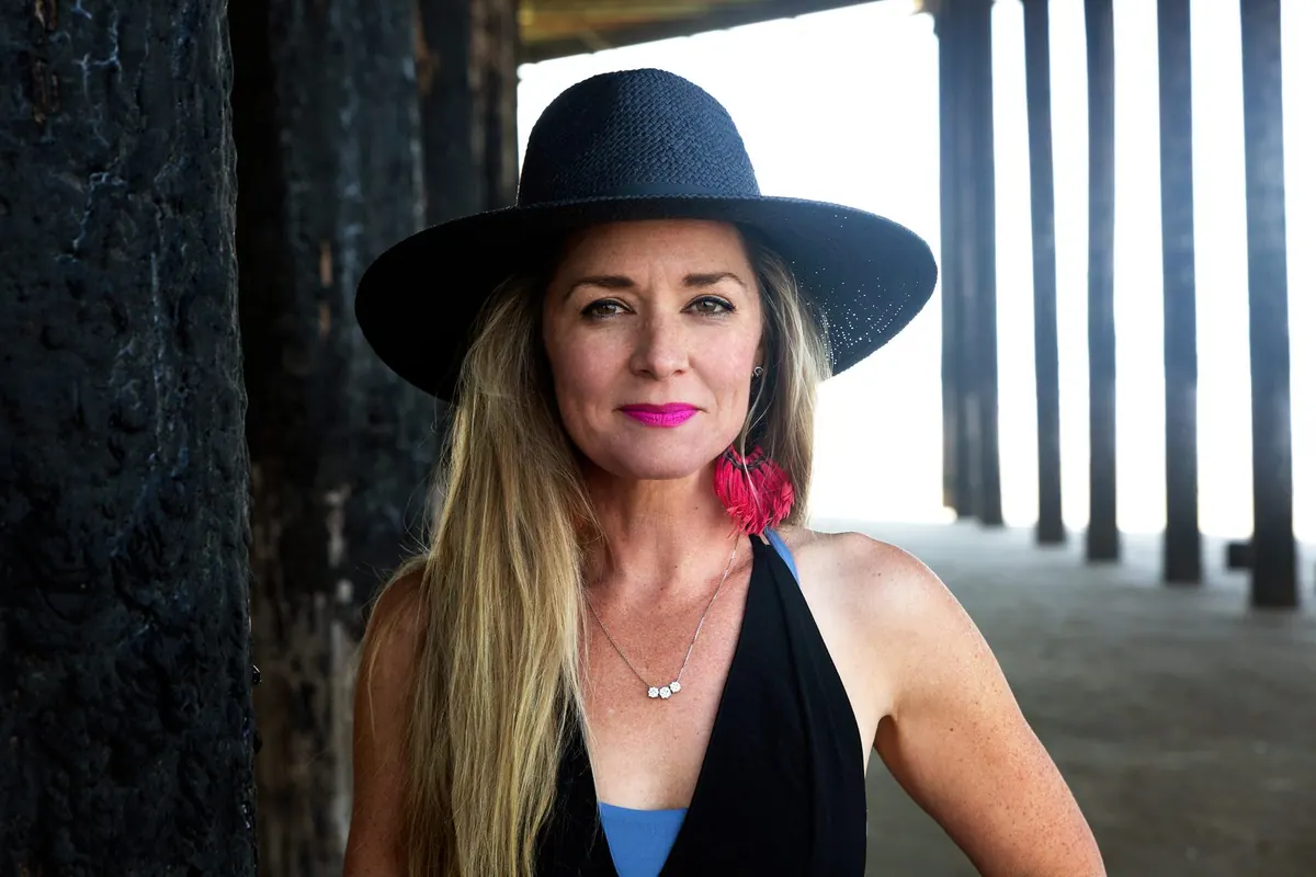 Anya Gossage in a black wide-brimmed hat by a beach pier