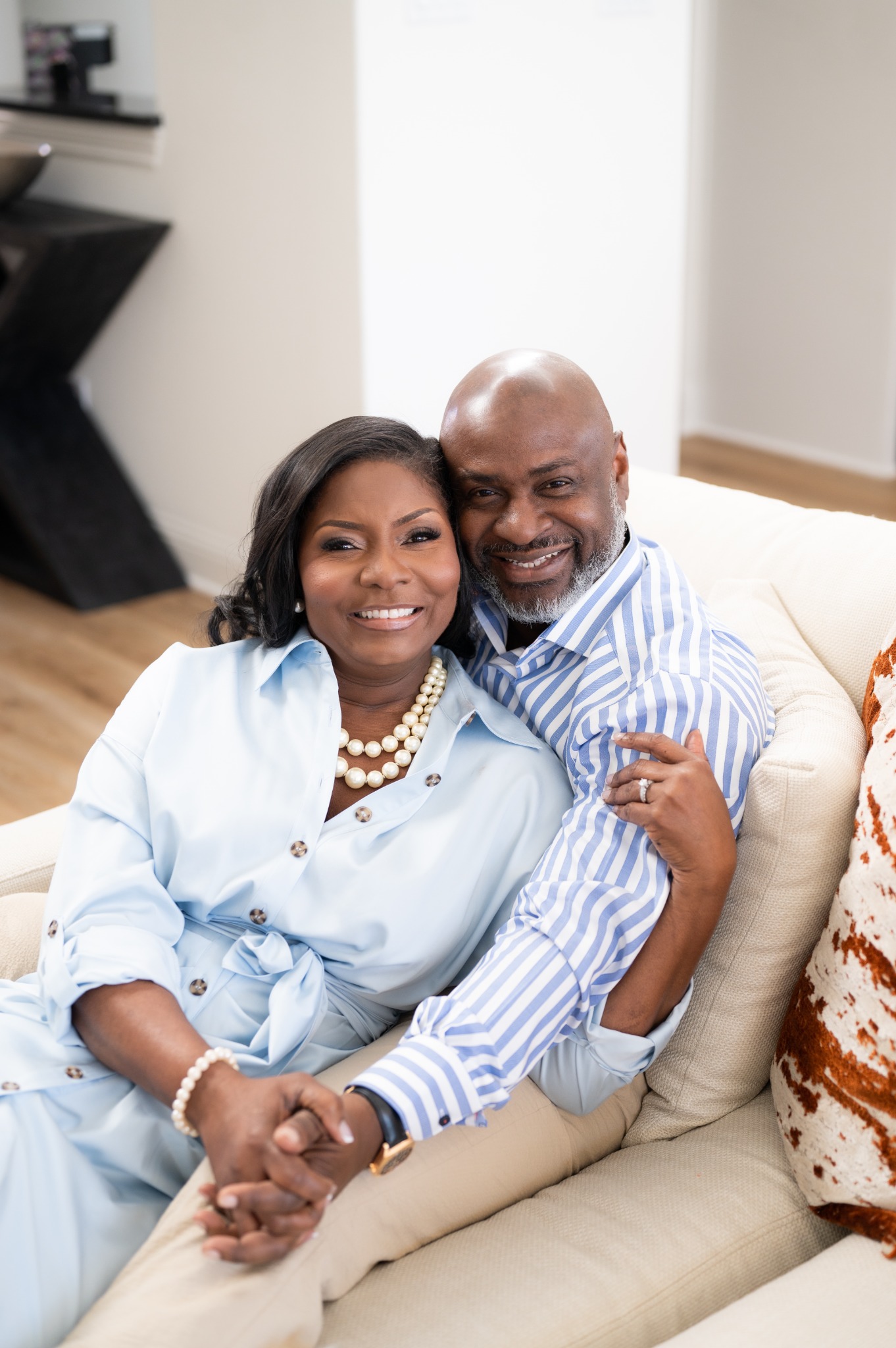 Michelle and Nigel seated together, smiling at the camera and holding hands