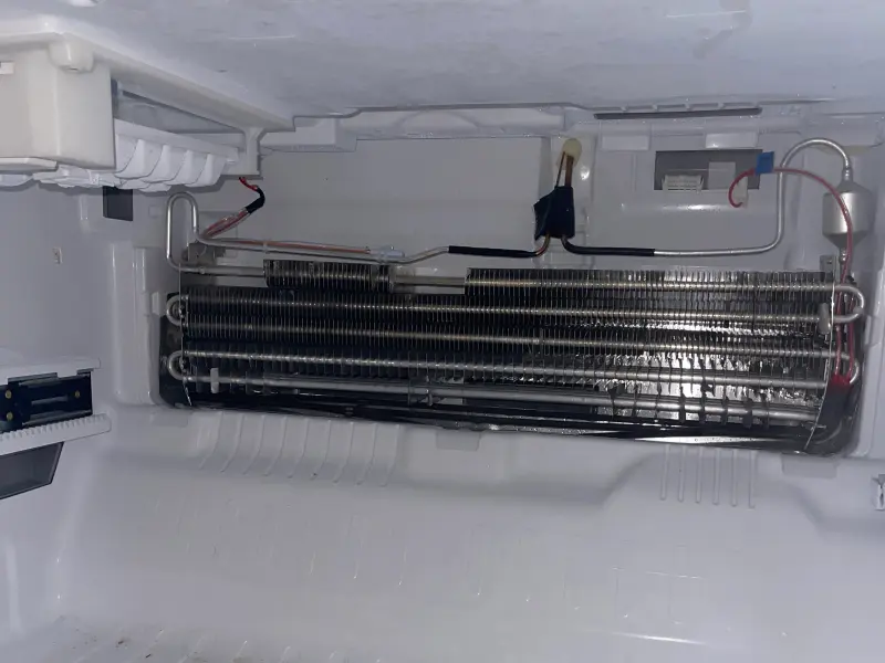Clean, frost-free refrigerator evaporator coil exposed for inspection in a Charlotte-area home