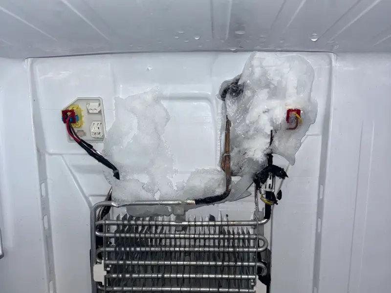 Frozen refrigerator evaporator coil with ice around the defrost wiring and tubing