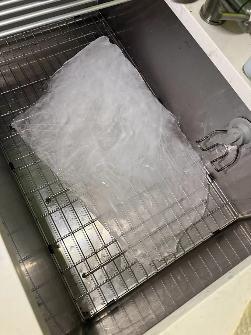 Large slab of ice removed from a freezer, resting in a kitchen sink