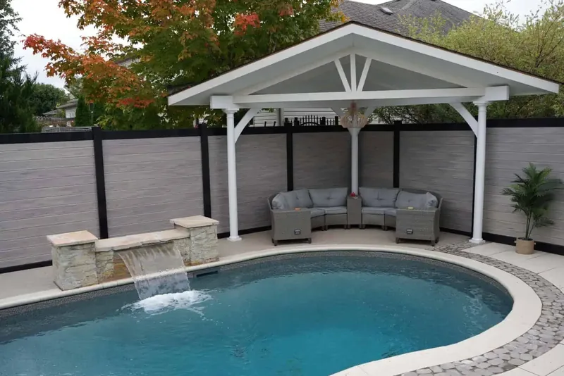 A grey composite privacy fence with black posts around a backyard pool and cabana, built by Elie's Fencing