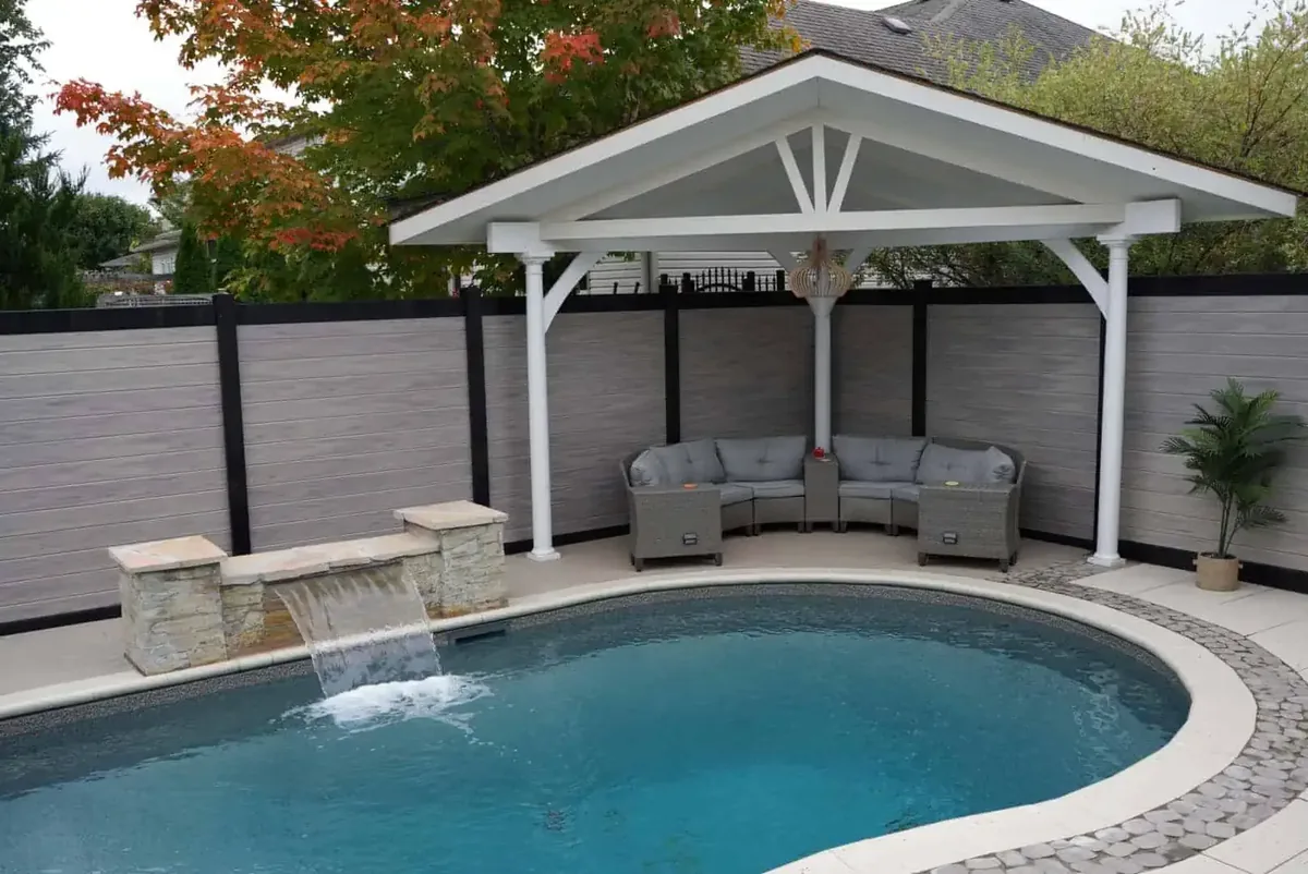 A grey composite privacy fence with black posts around a backyard pool and cabana, built by Elie's Fencing