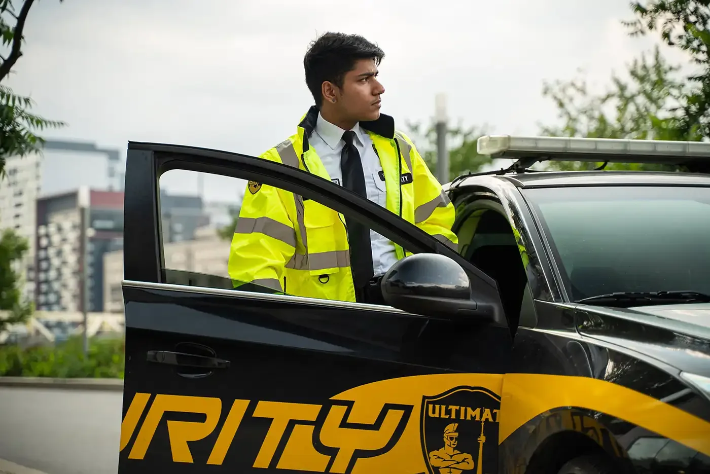 Security company marketing: an Ultimate Security guard in a high-visibility jacket stepping out of a marked patrol car