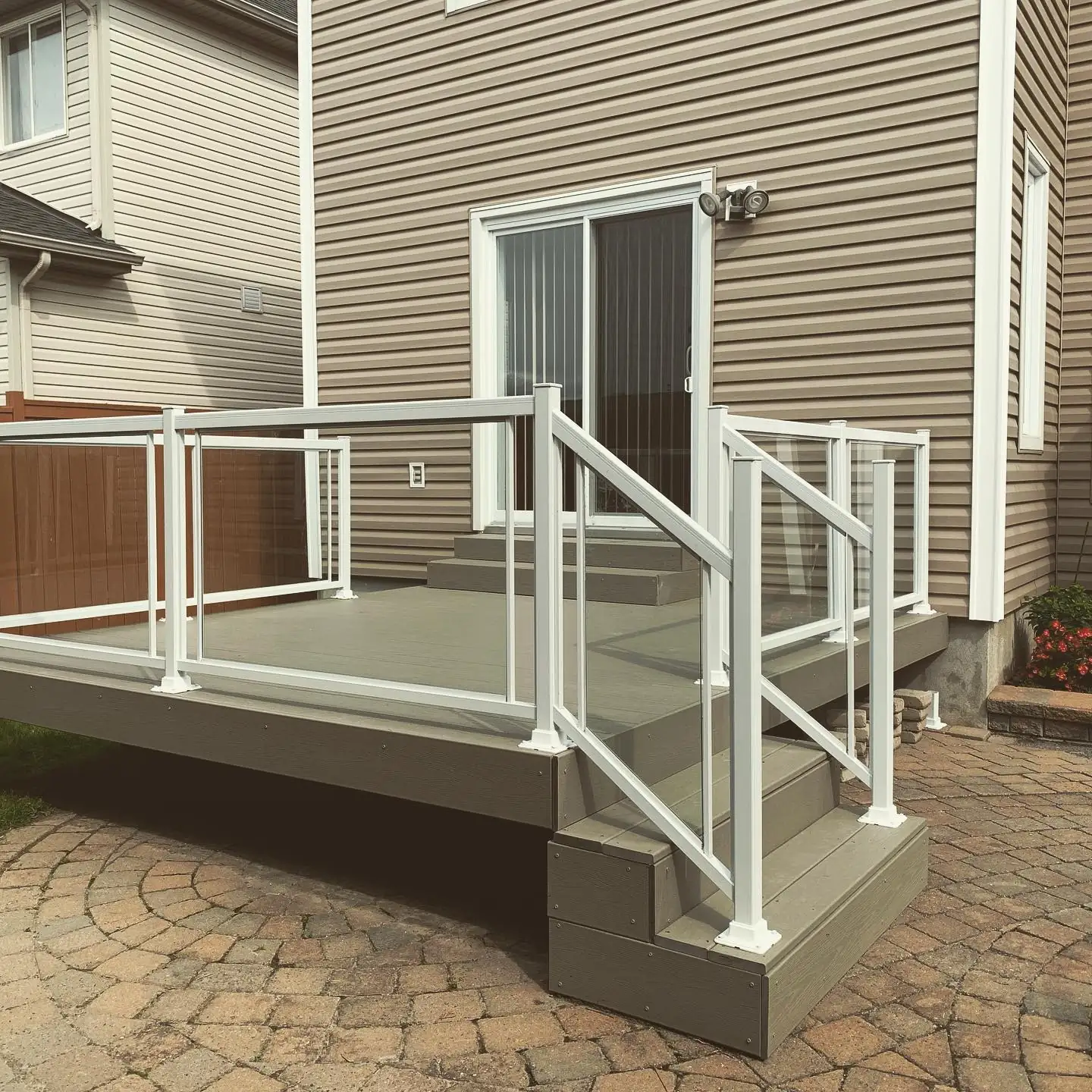 A grey composite deck with white-framed glass railings and stairs, built by Backyard Pros