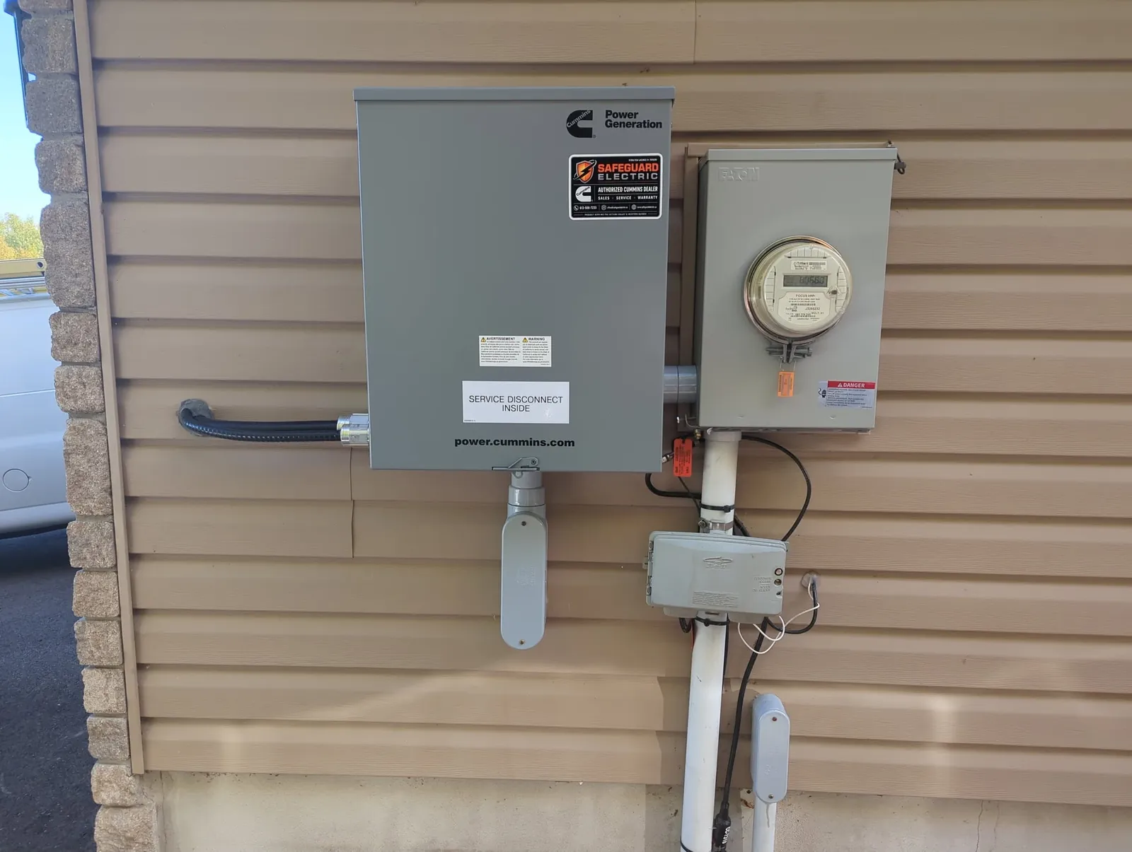 A generator transfer switch with the Safeguard Electric dealer sticker, mounted beside the hydro meter