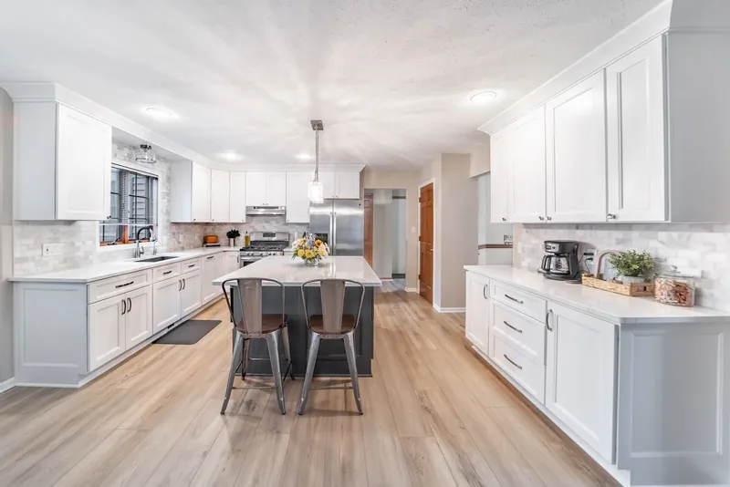 An open white kitchen with a dark grey island, marble subway-tile backsplash and light wood floors, from Kitchen Tune-Up