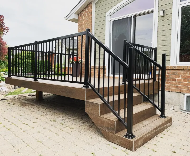 A composite deck with black aluminum railings and steps down to an interlock patio, built by Backyard Pros