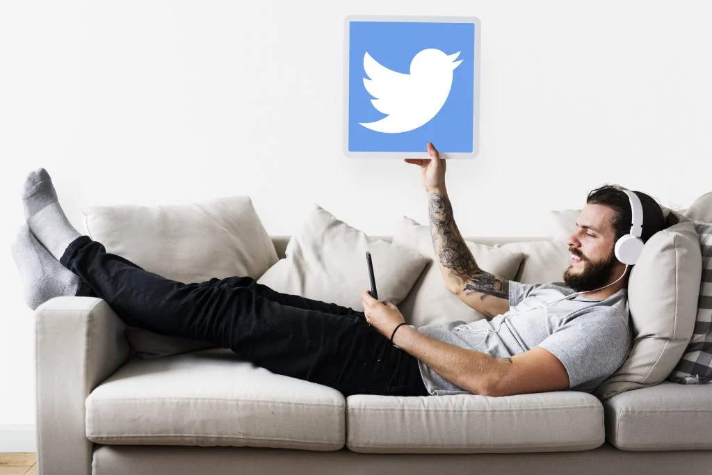 A man relaxes on a couch, headphones on, tablet in hand showcasing the Twitter logo—pondering how to pick the best social media platform for his needs, how to pick the best social media platform