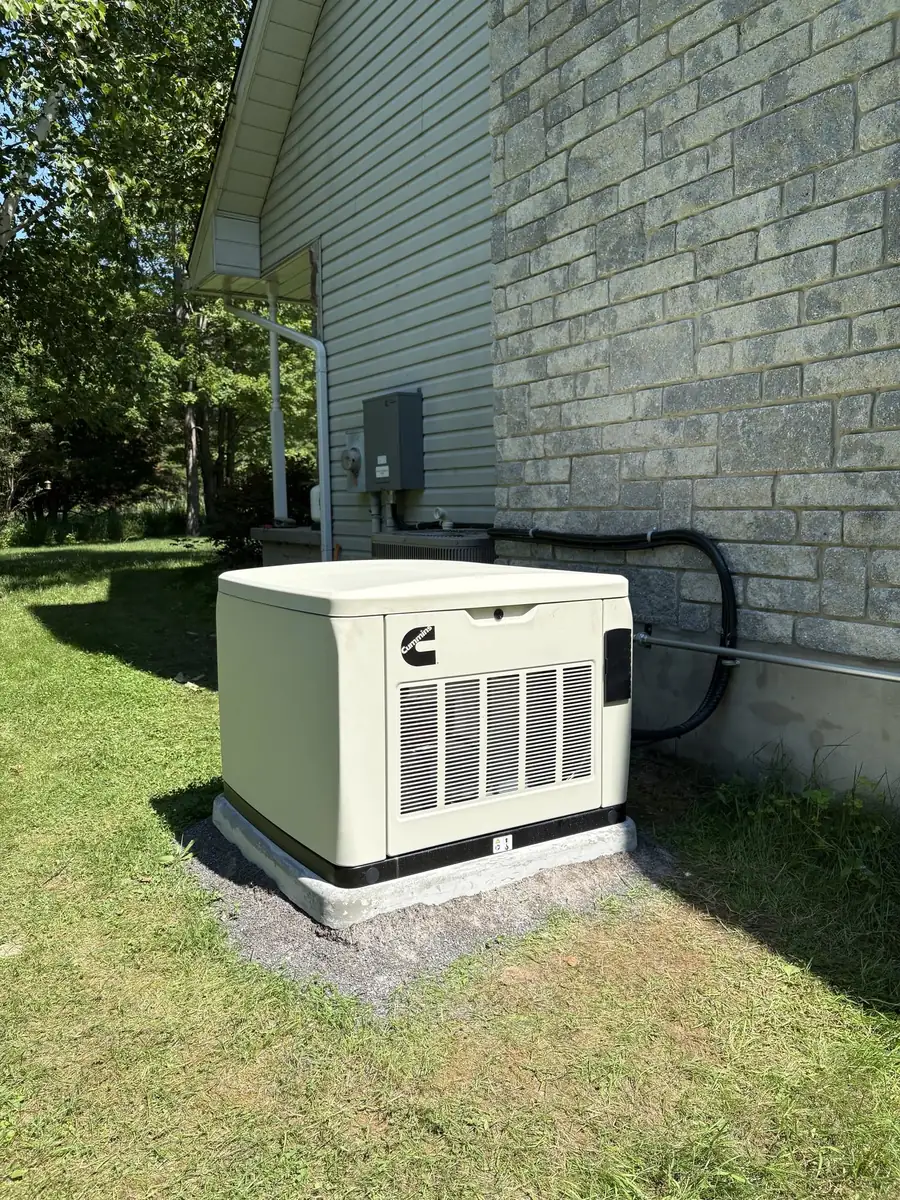 A standby generator on a concrete pad beside a stone house, installed by Safeguard Electric