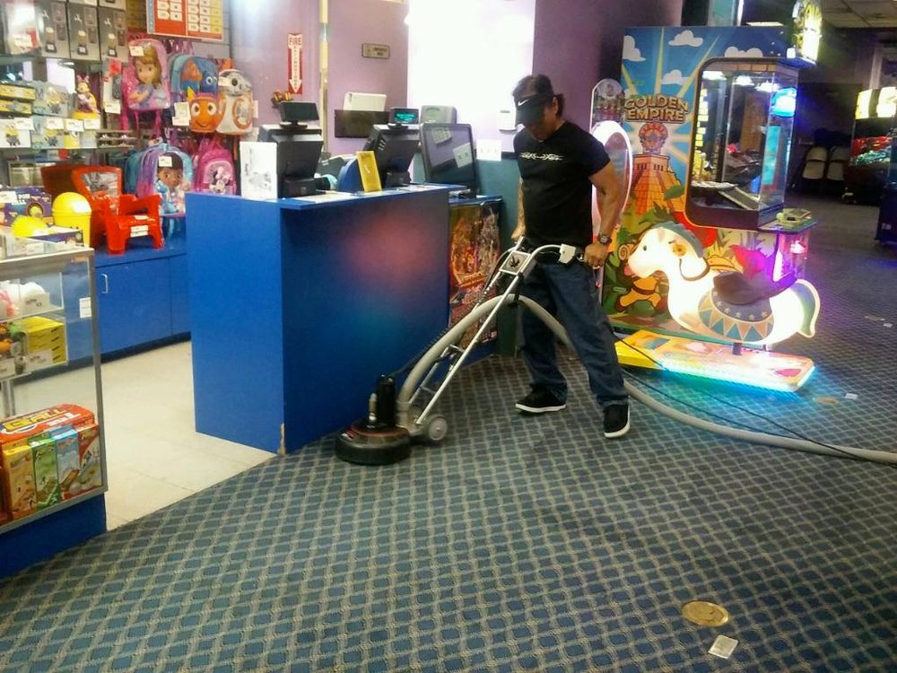 An employee using a powerful cleaning tool to clean an arcade.