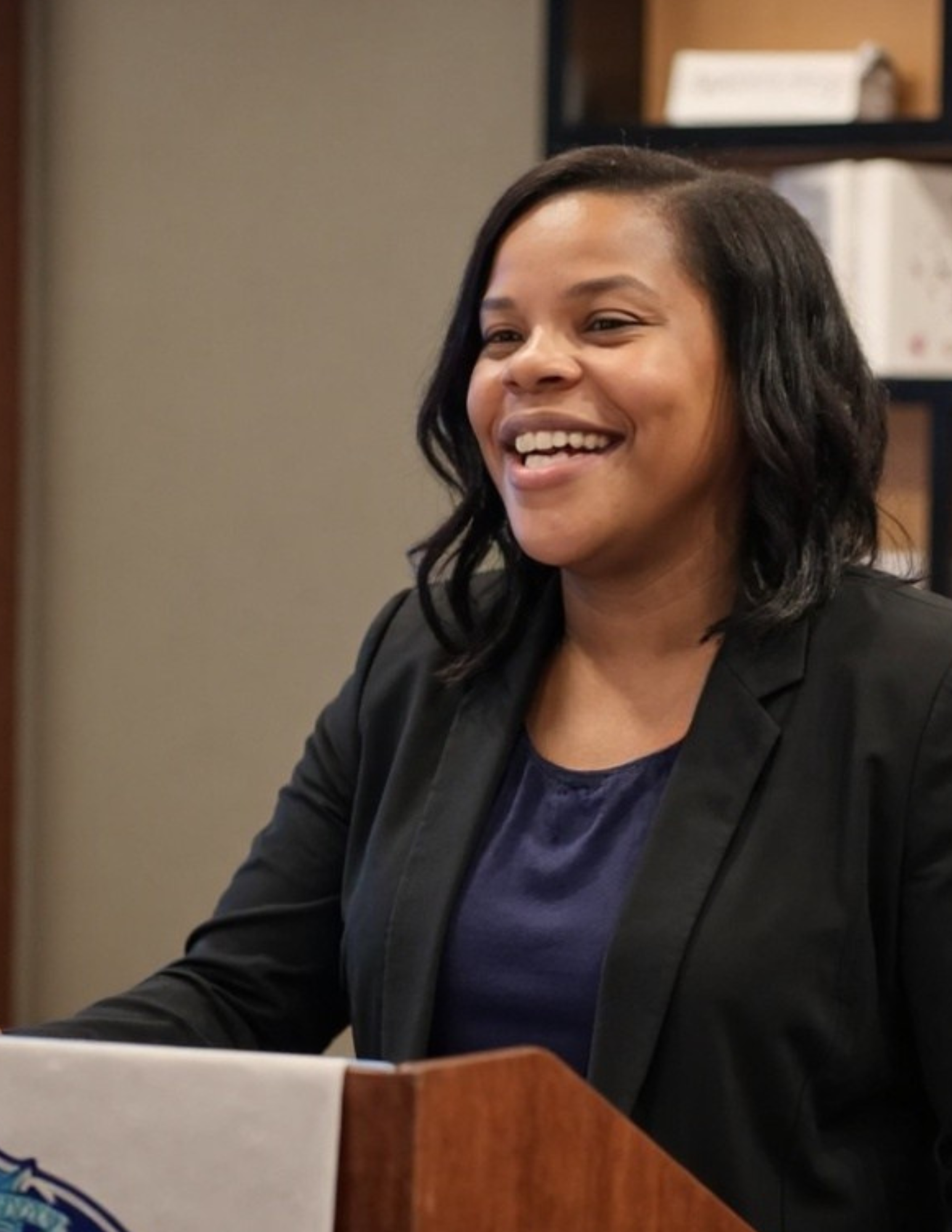 Sis. Natalie speaking, smiling warmly at the podium