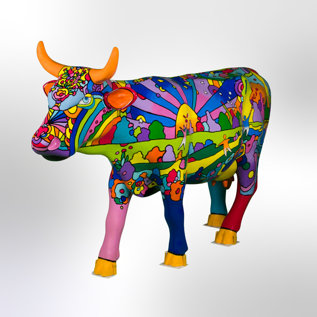 A brightly painted cow sculpture in a pop art motif style depicting spacious grounds with plants and people having fun in a park