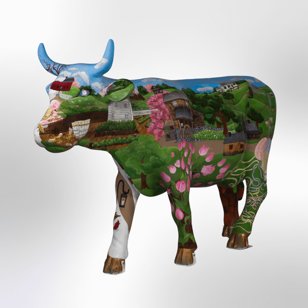 A coloful cow depicting historial buildings, flowers, grasslands, farm animals, gardens, and other sites of Old Sturbridge Village