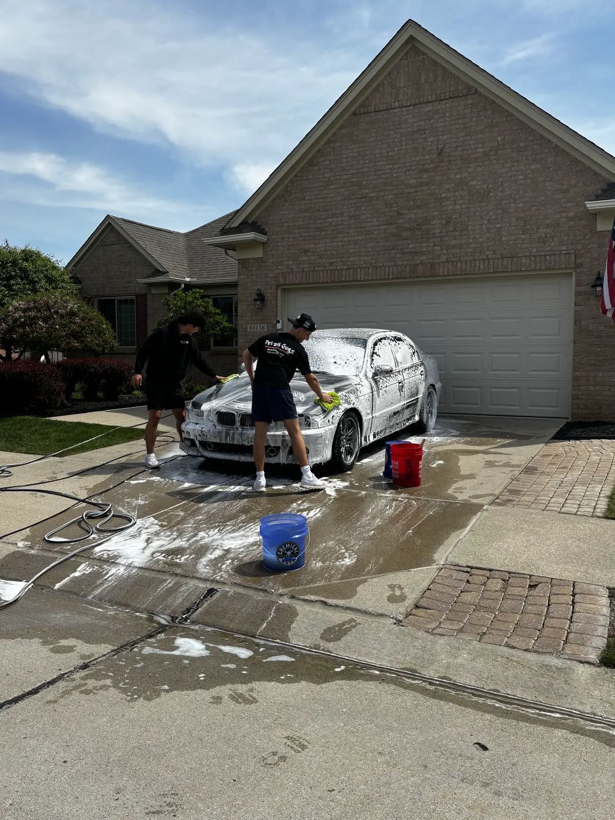 Two Detail Guyz technicians foam washing a car in a Macomb driveway