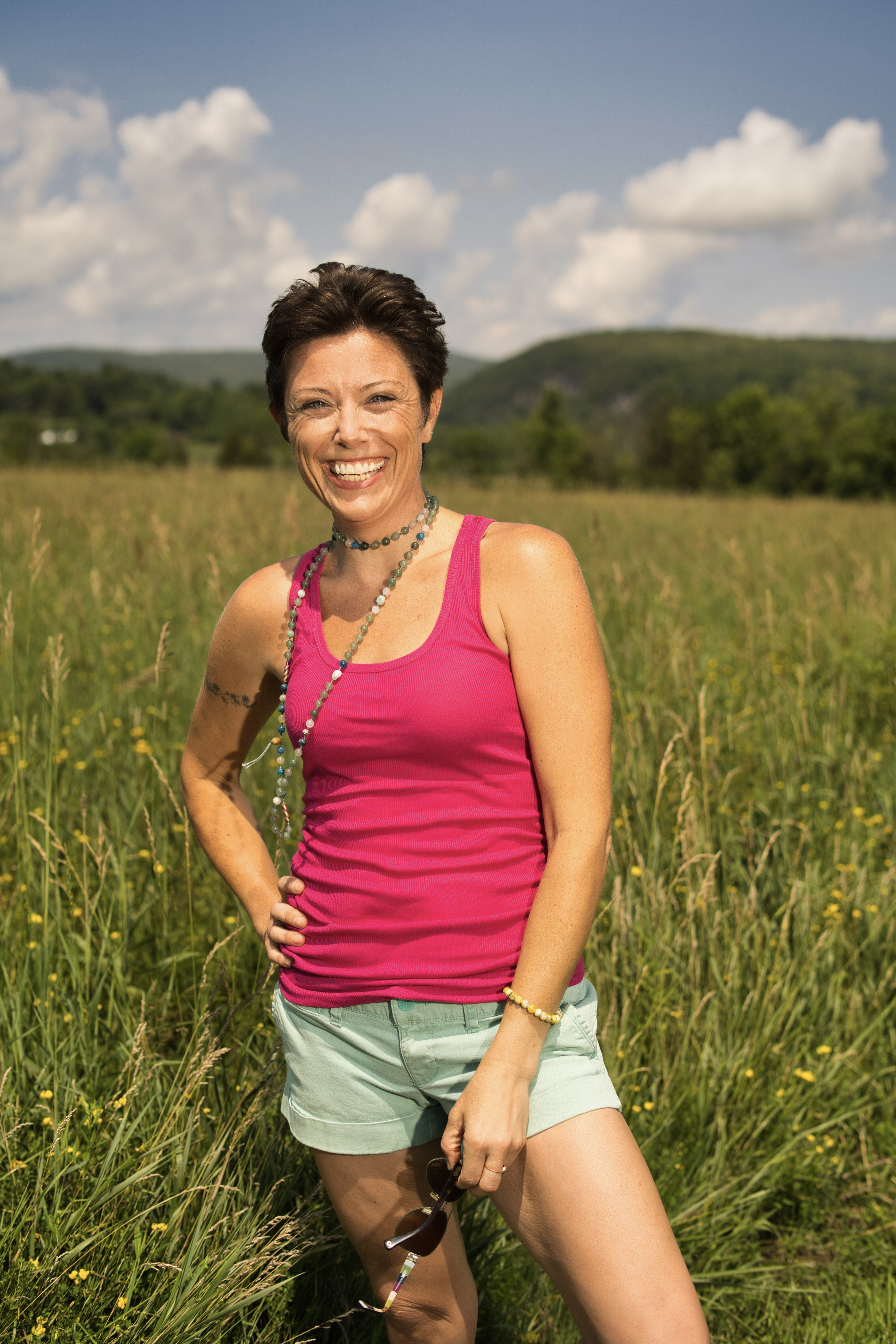 Marlaina smiling in a sunlit meadow with mountains in the distance