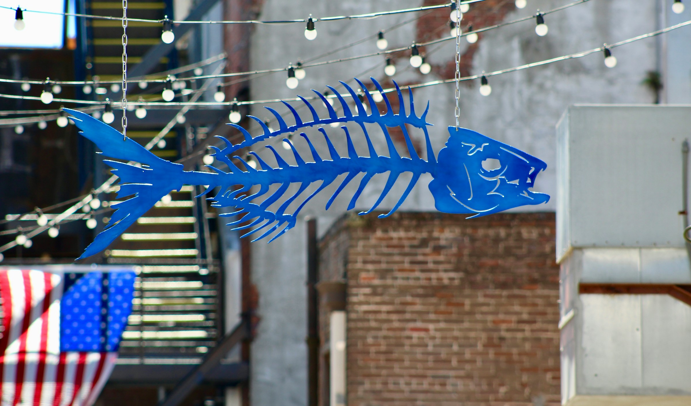 Blue metal fish skeleton sculpture hanging under string lights in Fishbone Alley, Gulfport