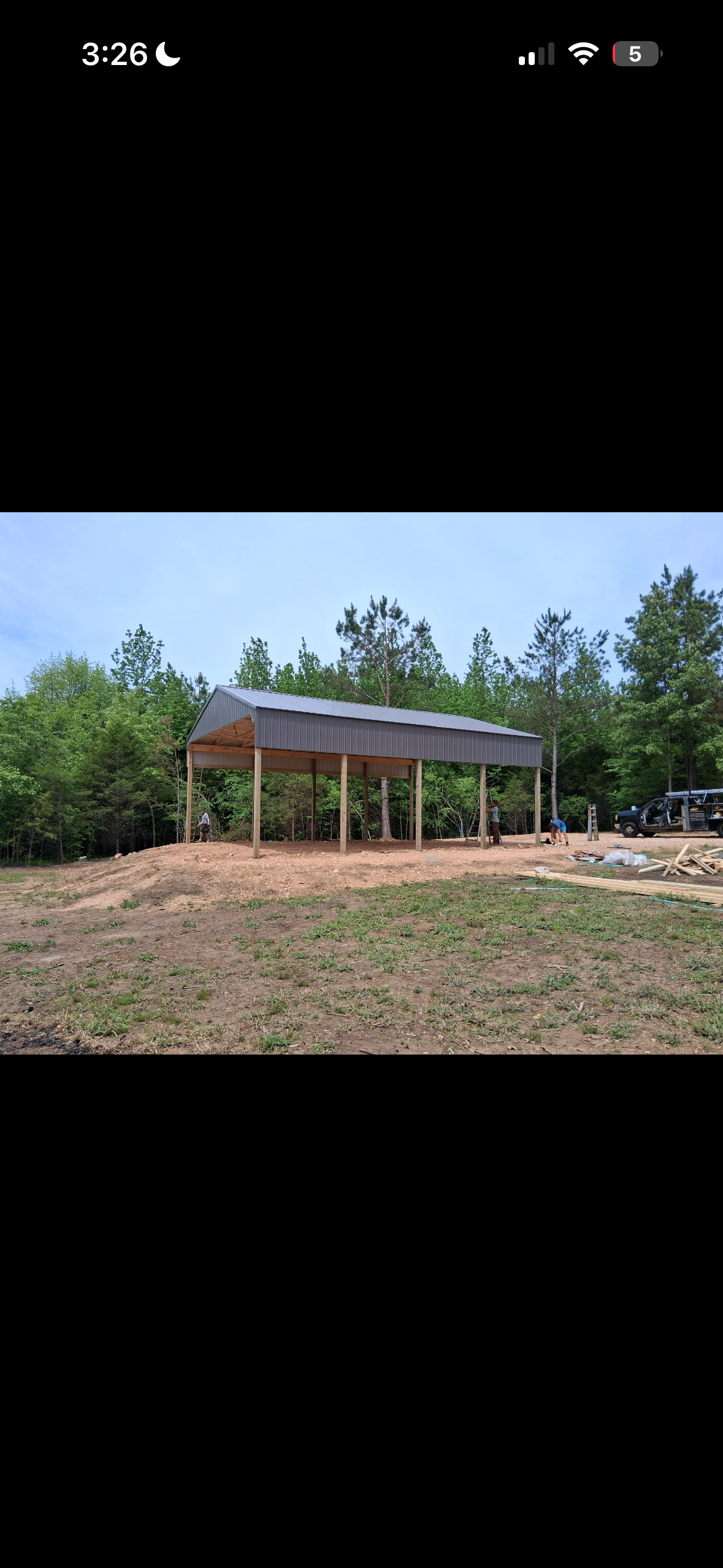 Open-sided pole barn with heavy timber posts and clear-span roof trusses under construction