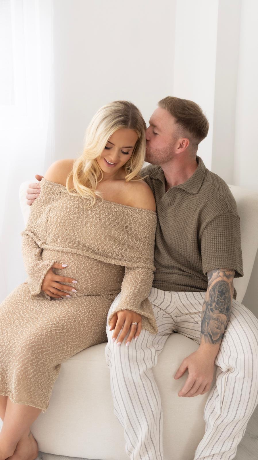Expecting couple on a cream sofa, he kisses her head