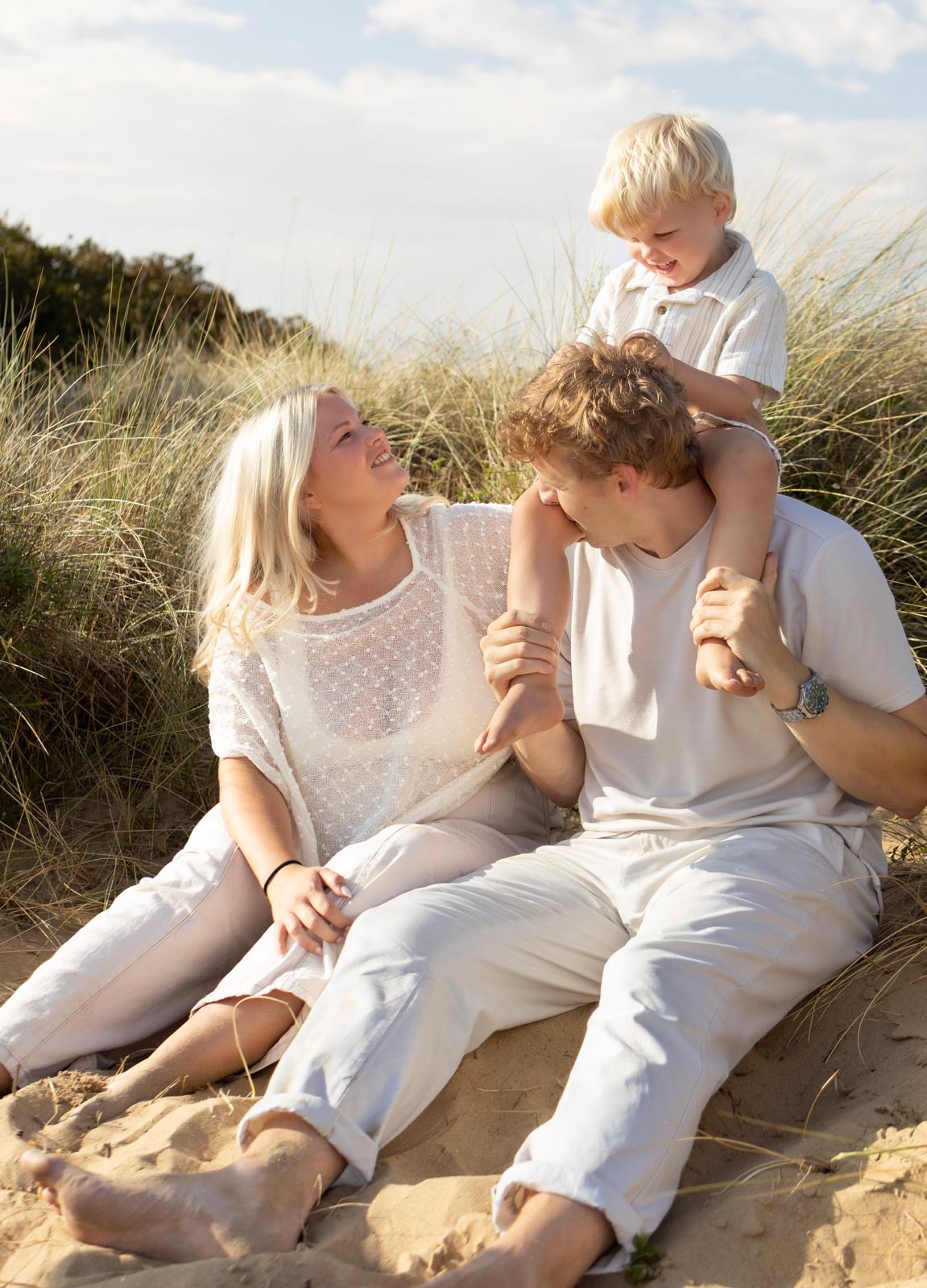 Family sitting in the sand dunes with their son on dad's shoulders