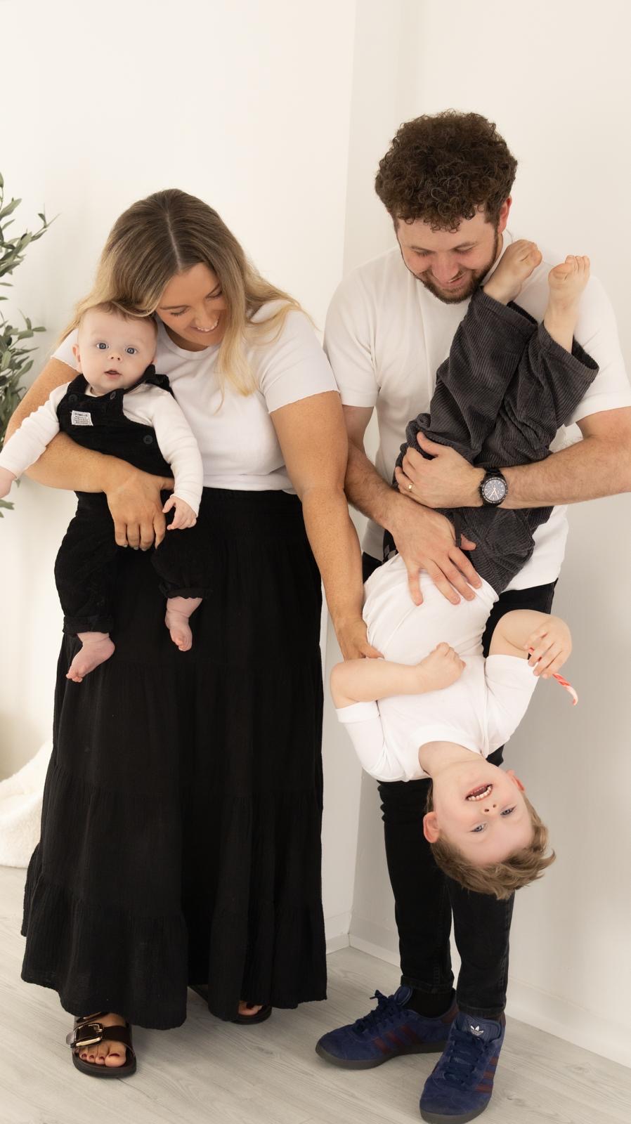 Family laughing as dad holds their toddler upside down