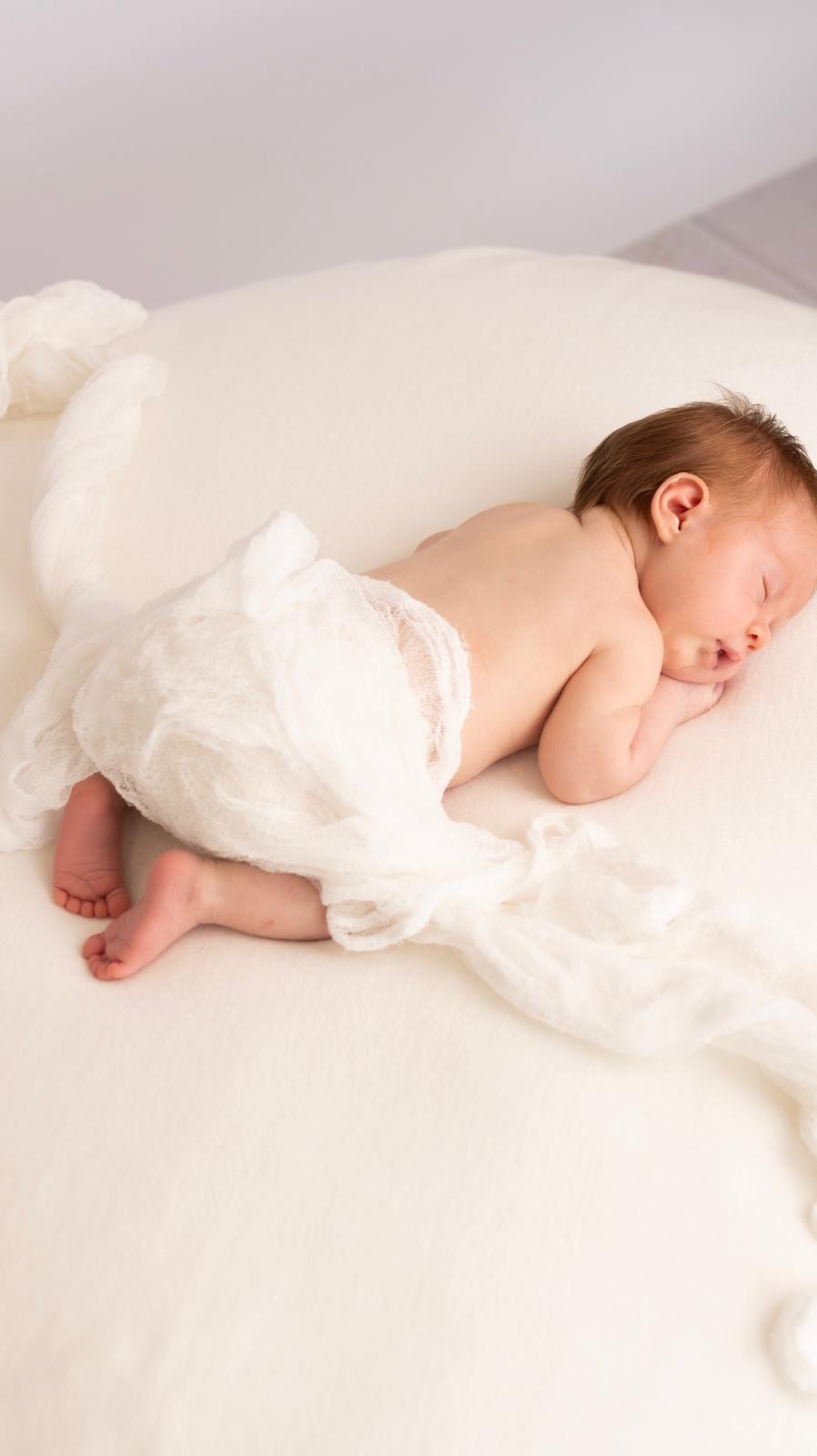 Newborn sleeping on a cream blanket with soft wrap