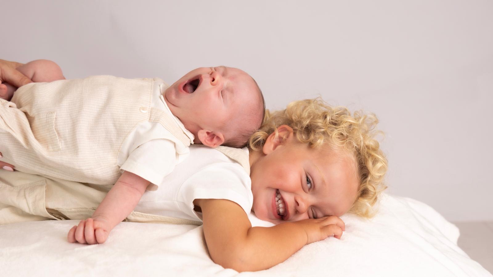Toddler grinning while his newborn sibling yawns on his back