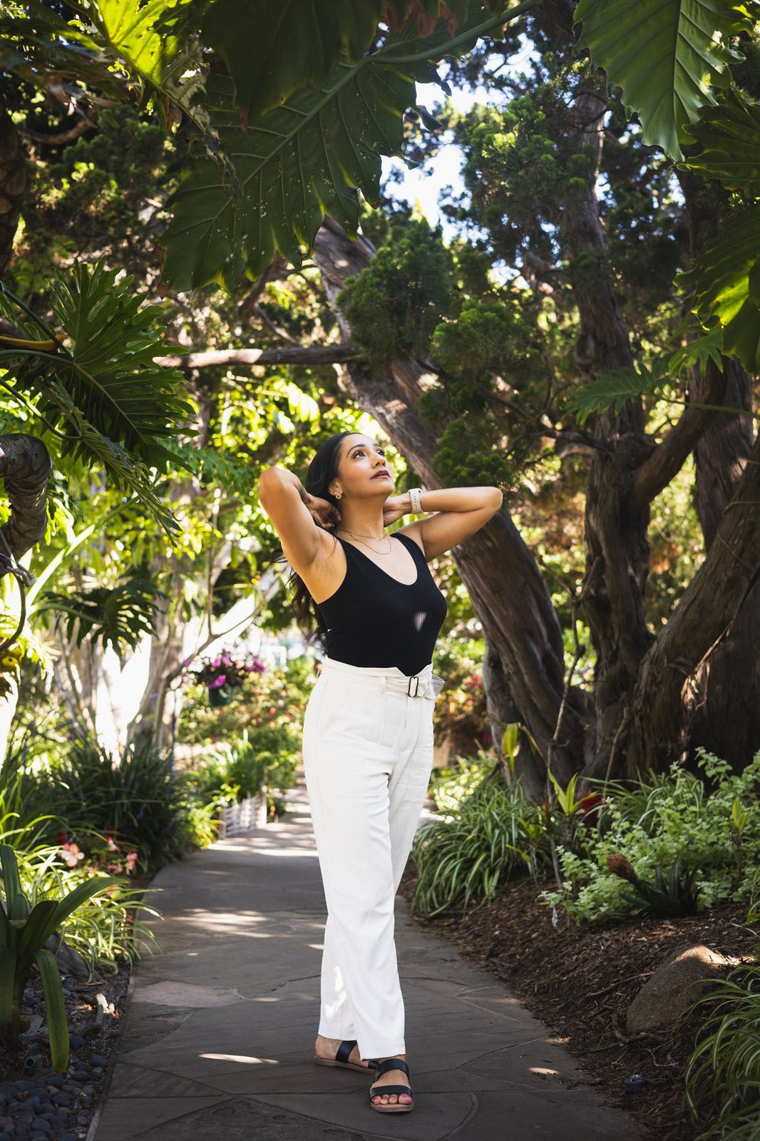 Andrea on a garden path beneath tall trees, looking up