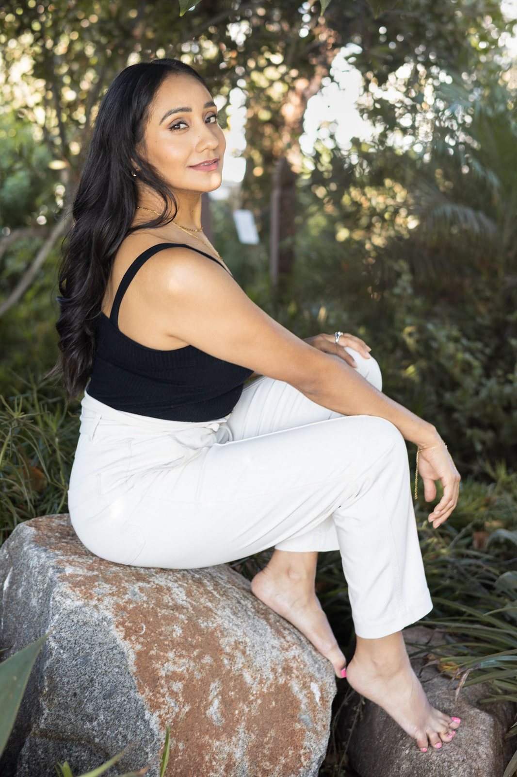 Andrea seated on a rock in a garden, looking softly to the side