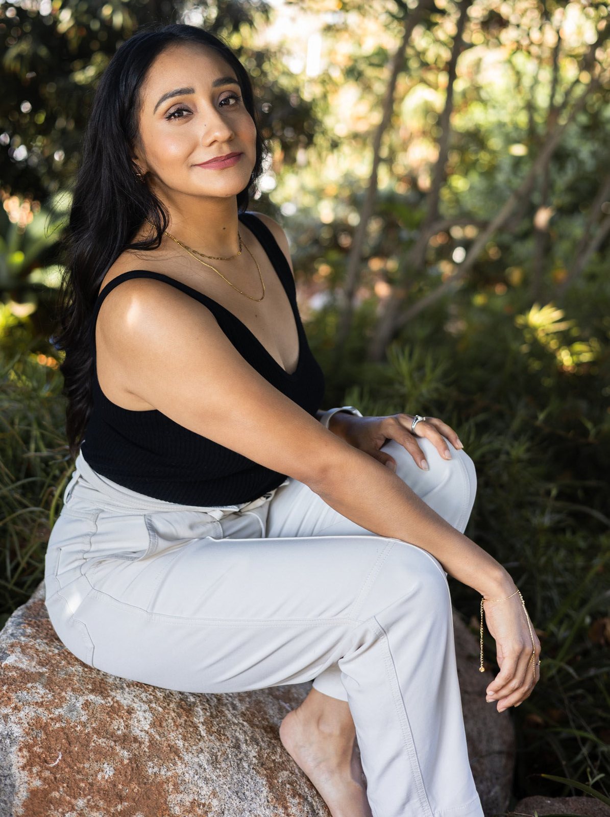 Andrea Arroyo seated on a rock in a garden, looking confidently at the camera