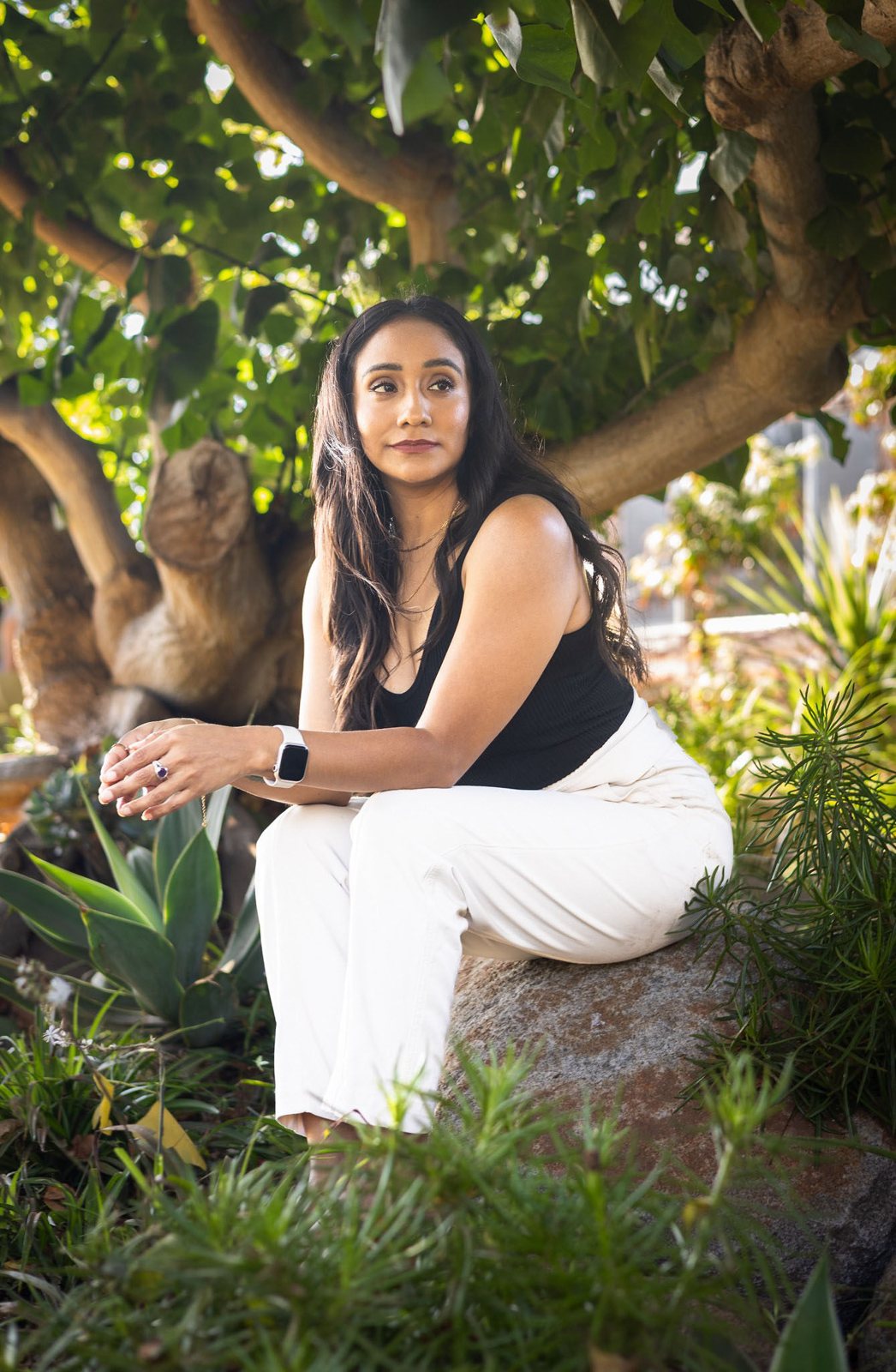 Andrea seated on a rock beneath a large tree, looking into the distance