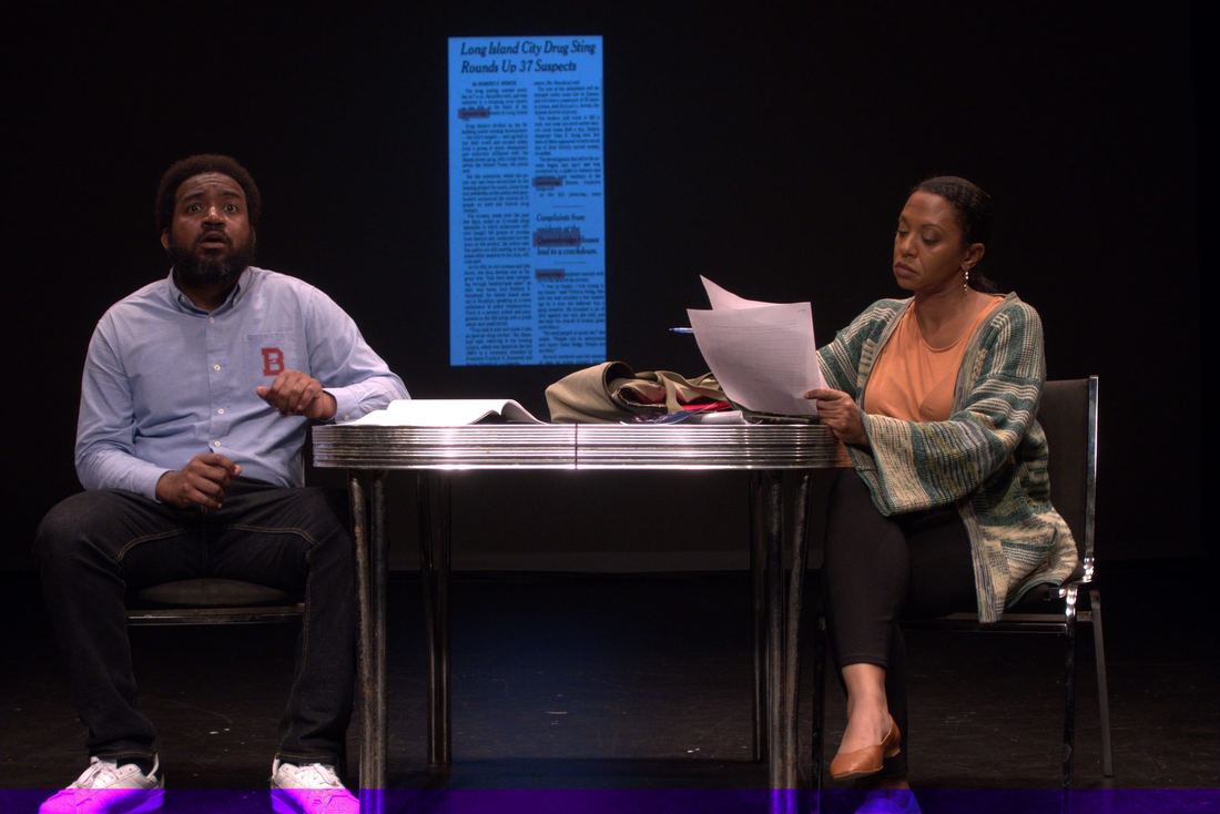Two actors at a reading table with a projected notice