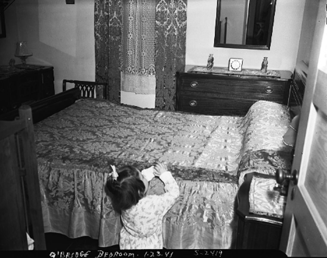 Child beside a neatly made bed, 1941