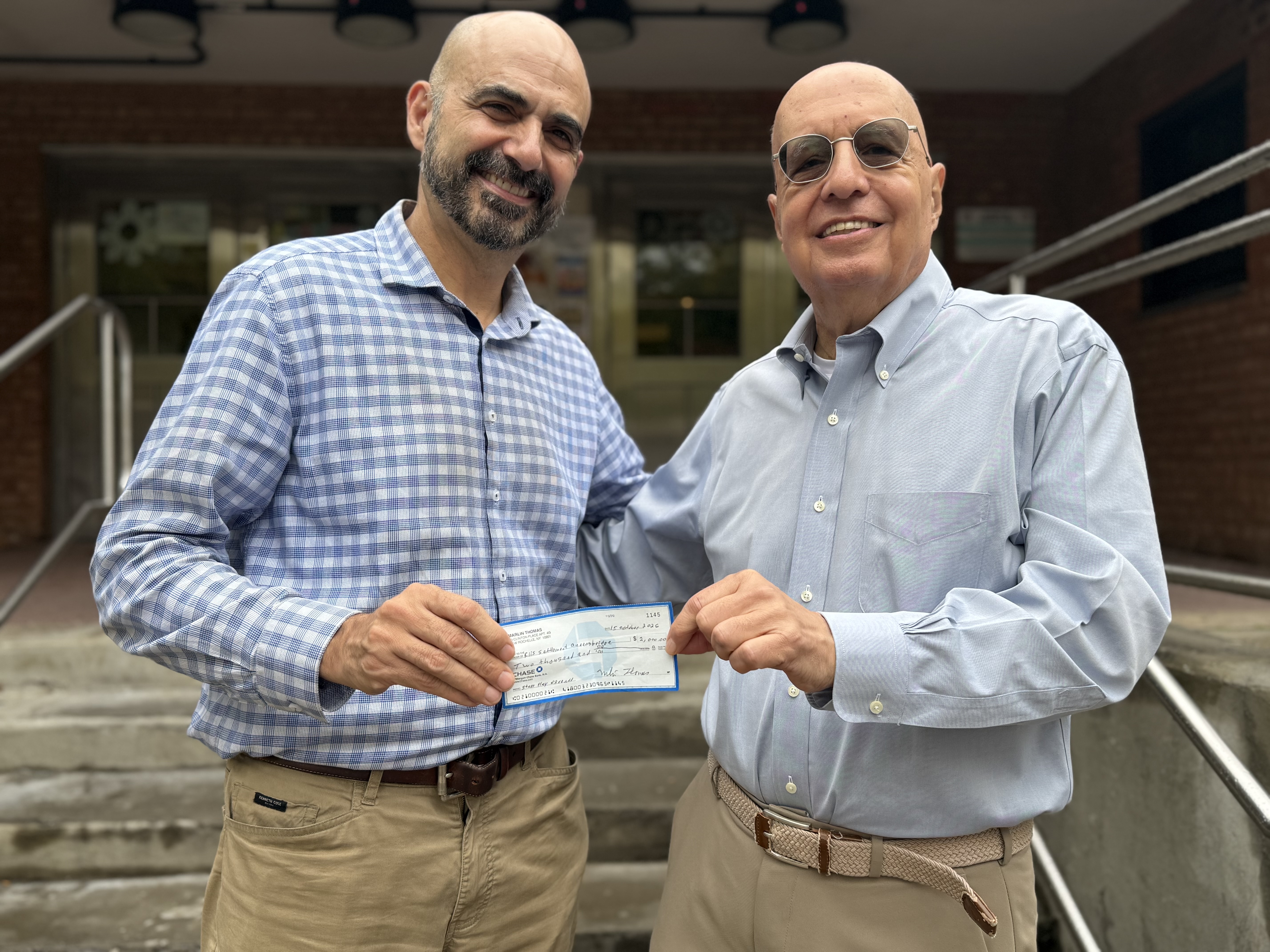 Marlin Thomas presenting a check to Chris Hanway outside the Jacob A. Riis Settlement House