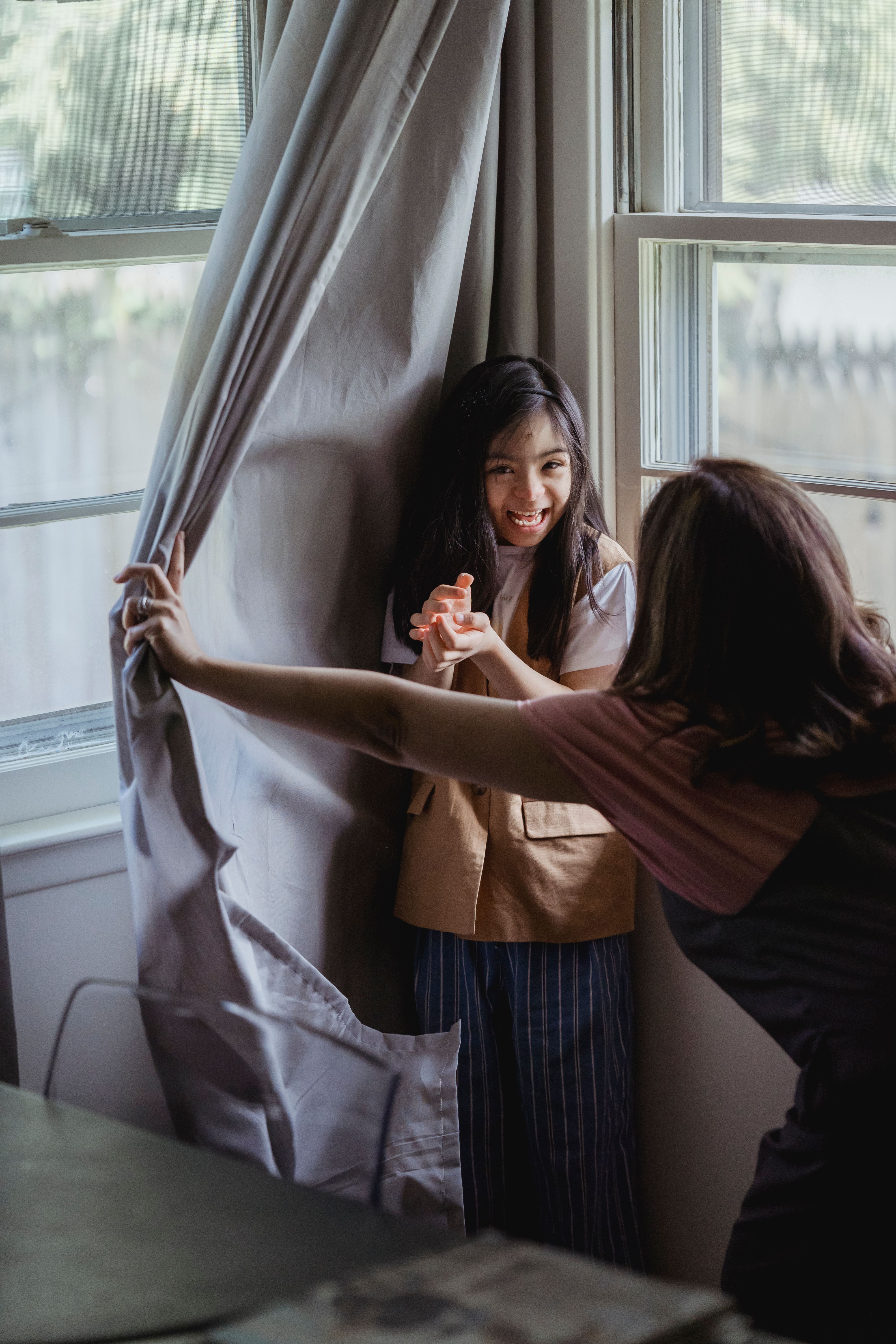 Child playing peekaboo from behind a curtain with a parent