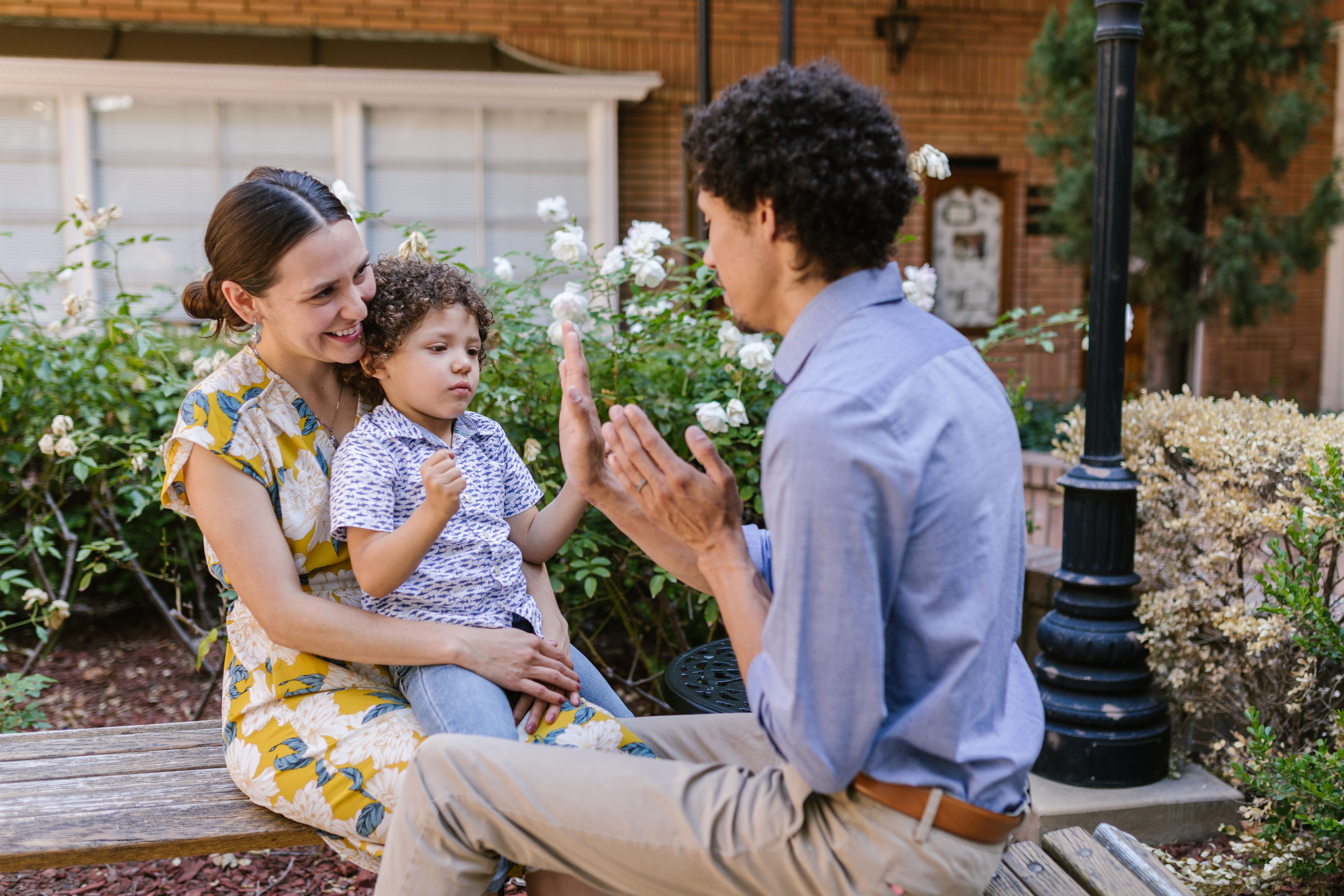 An adult modelling a hand gesture while a child sits on a parent's lap