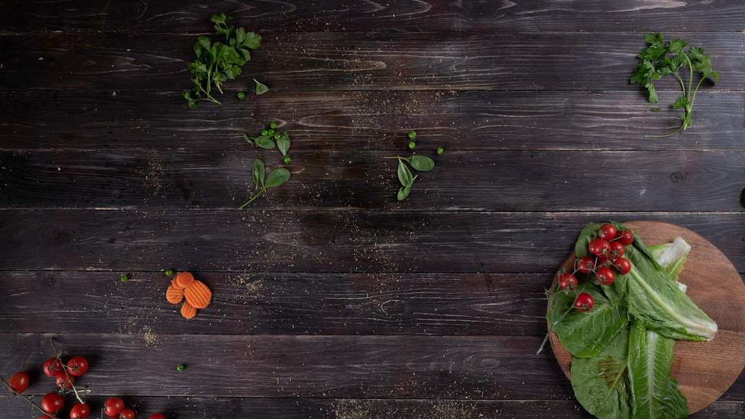 Overhead view of fresh romaine, cherry tomatoes, carrots and herbs scattered on a dark rustic wood table.