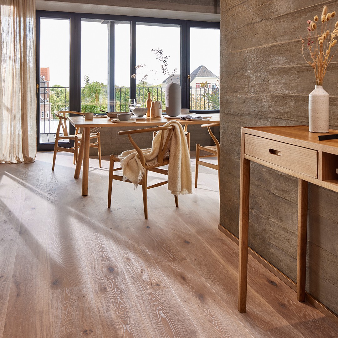 Modern dining area featuring wood flooring, natural light from large windows, wooden dining table with tableware, minimalist decor, and a cozy atmosphere.