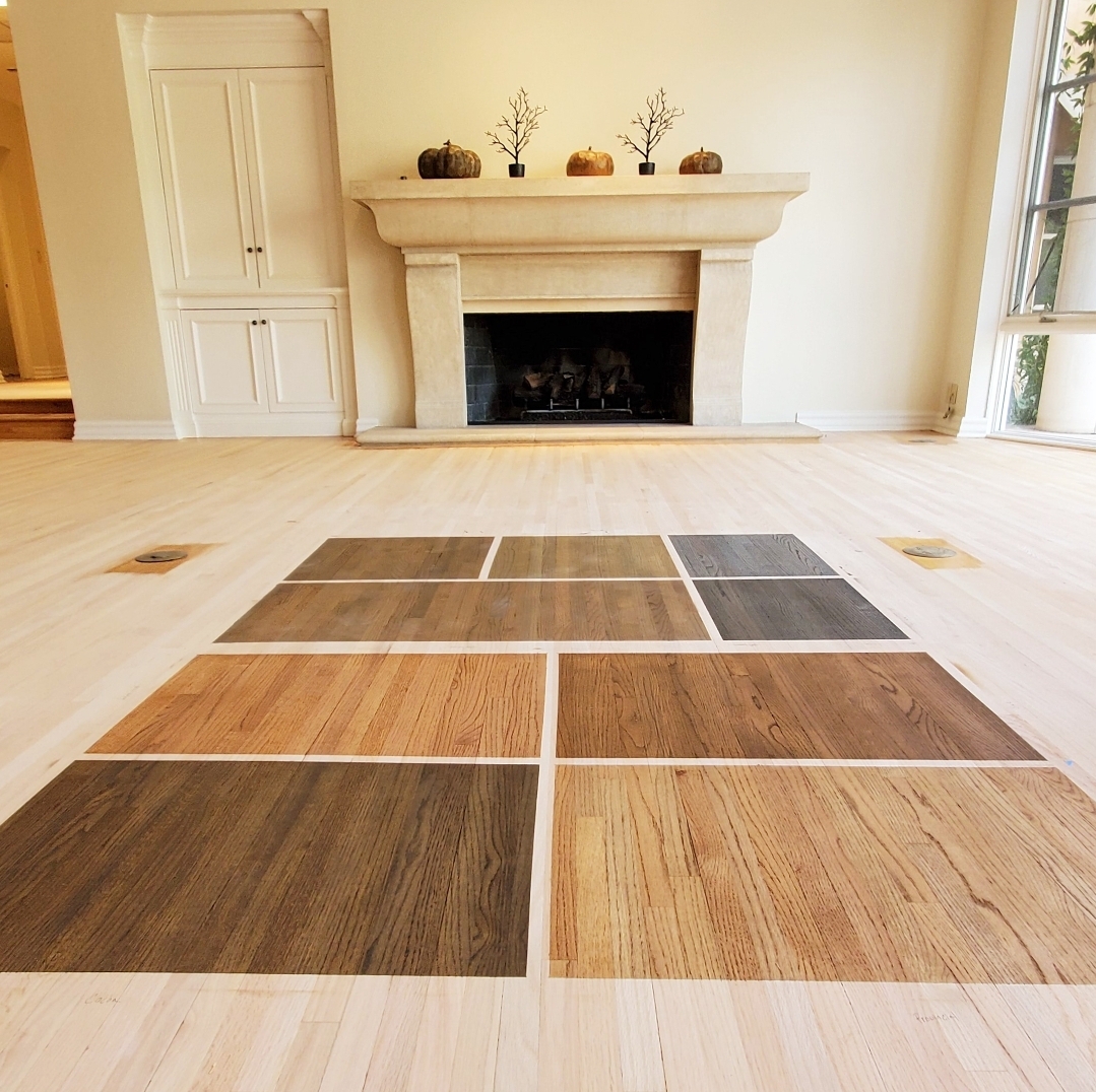 Wood floor sample swatches displayed on a light hardwood floor in a spacious room with a stone fireplace, showcasing various stain options for custom finishes at AZ Floor Haven.