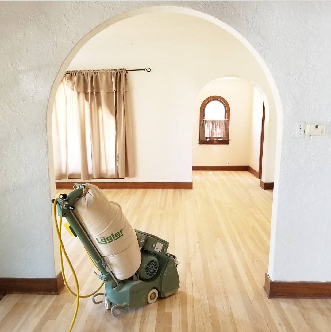 Wood floor refinishing equipment positioned in a bright, empty room with polished hardwood flooring, showcasing the preparation for expert restoration services by AZ Floor Haven.