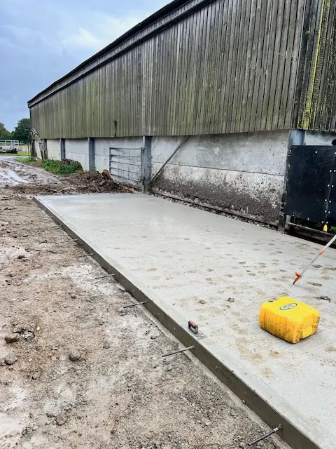 Freshly poured concrete base beside a farm building