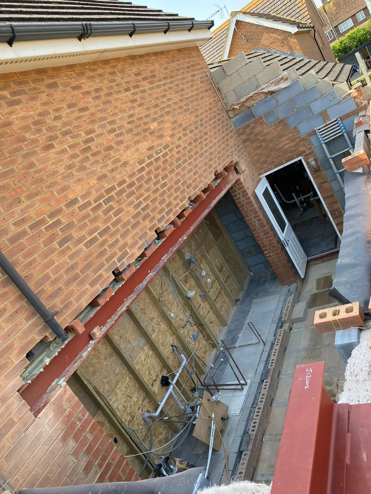 Red steel beams fixed against brickwork for an extension