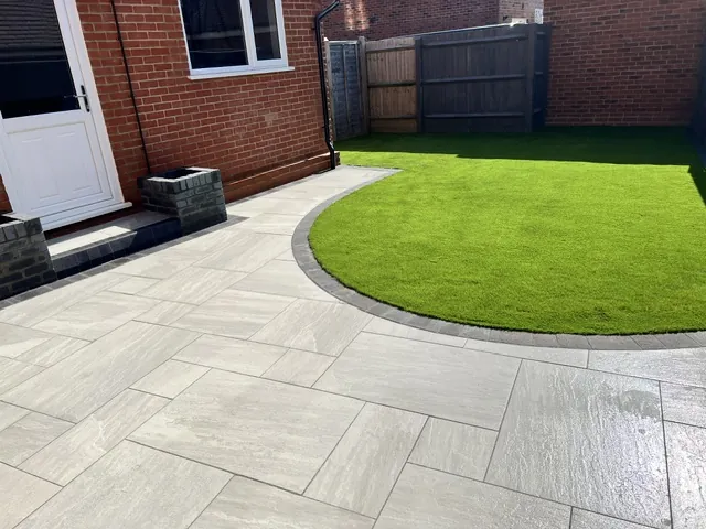 Pale paved patio with dark edging around a curved lawn