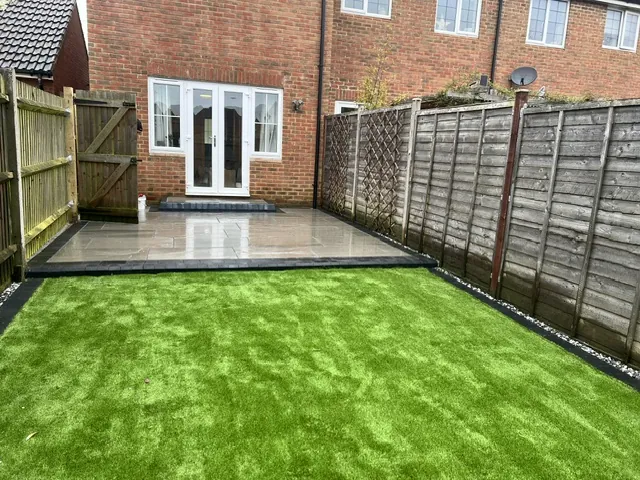 Grey paved patio and lawn in a fenced back garden