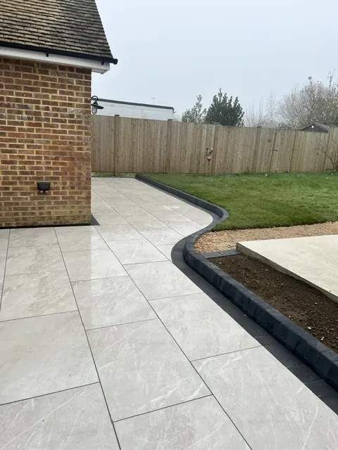 Pale paving with a curved dark edge beside a bungalow lawn