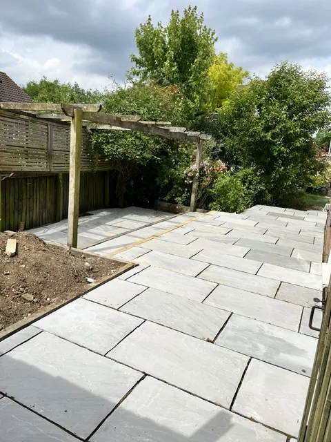 Grey stone patio with a timber pergola in a back garden