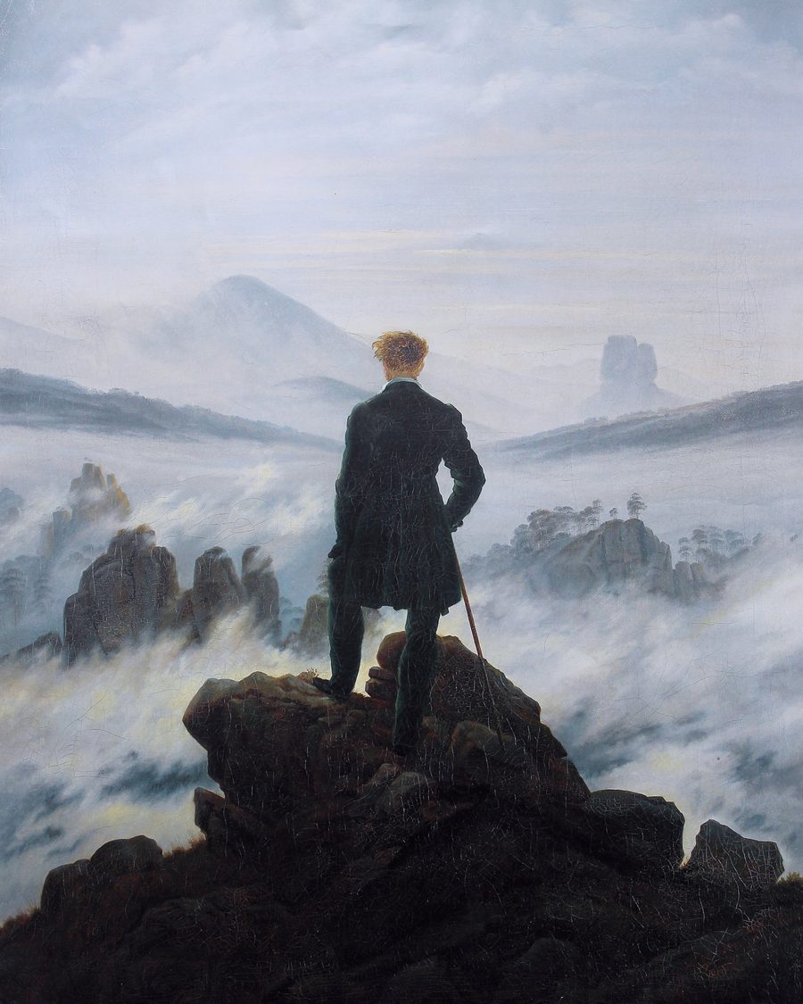 A man seen from behind on a rocky summit, looking over a sea of fog