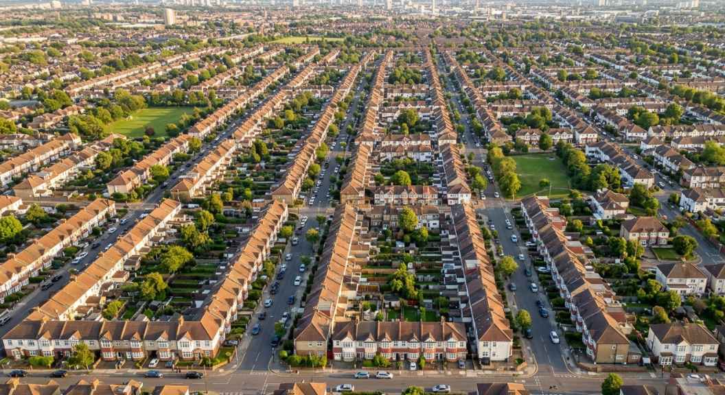 An aerial view of London's outer suburbs showing streets of semi-detached and terraced houses, warm afternoon light, photorealistic, no text, no logos, UK residential neighbourhood An aerial view of London's outer suburbs showing streets of semi-detached and terraced houses, warm afternoon light, photorealistic, no text, no logos, UK residential neighbourhood